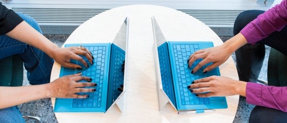two people at a round table typing on blue coloured laptops