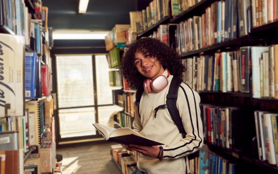 Middle years student in library with headphones around neck and a book.